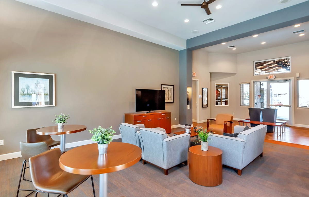 Community lounge with television, seating and round tables.