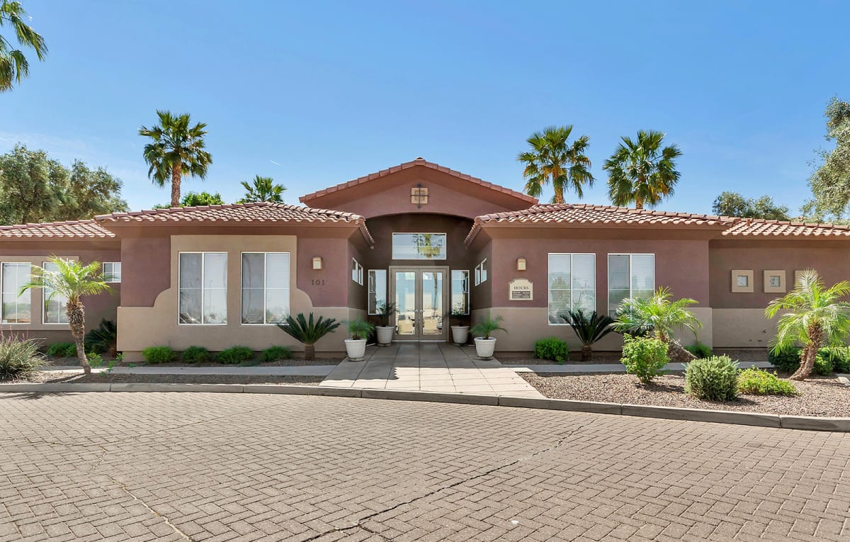 Clubhouse entrance with palm trees and a paved approach.