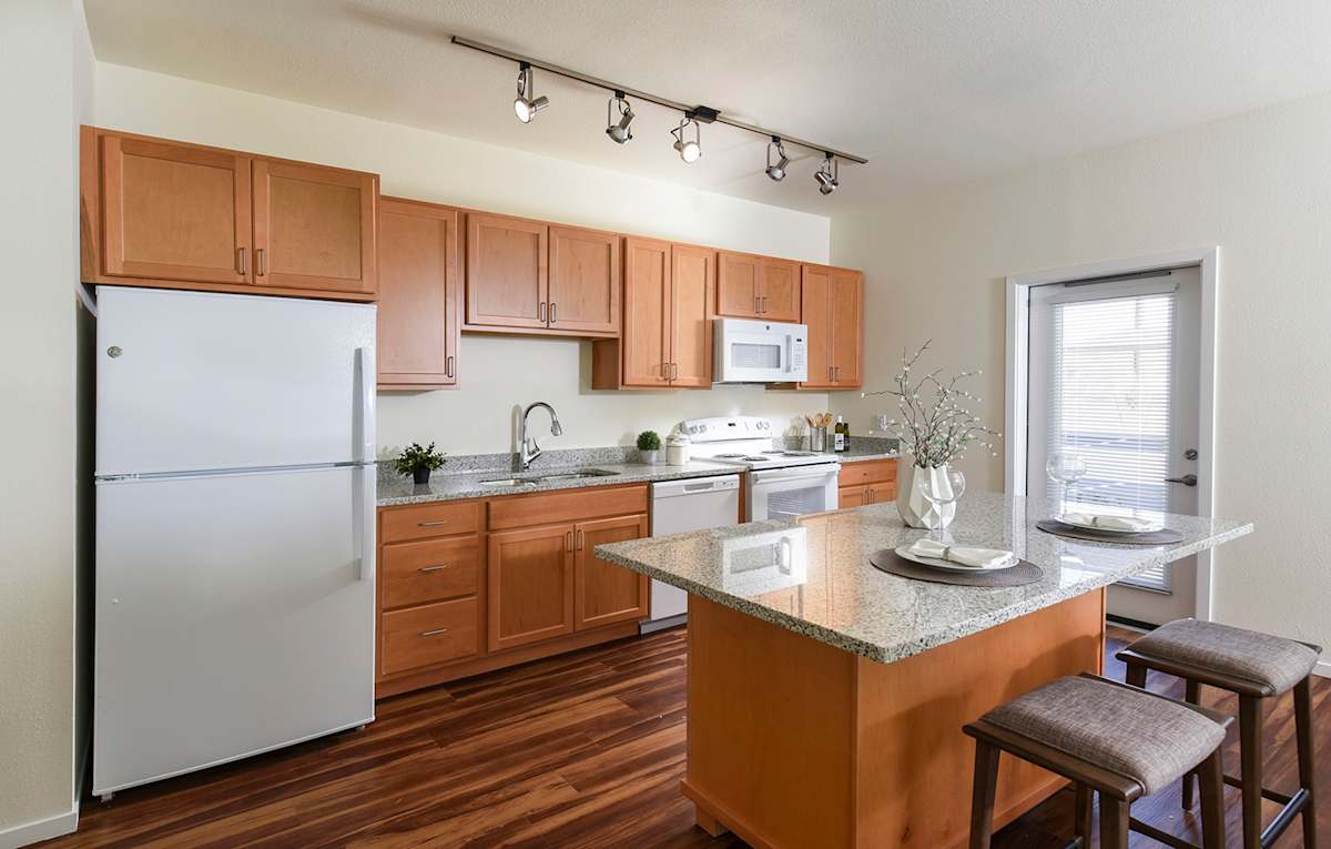 Kitchen with wood cabinets and island seating — view 1 at Juniper Square 55+ Apartments.