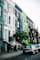 A street with cars parked on the side and a green tree in front of a building.