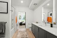 Studio Apartments in Sacramento, CA - The Eisley - Large Bathroom with Wood-Inspired Plank Flooring, Vanity with Grey Cabinets and Large Mirror with Built-In Lights, and Shower and Bathtub Combo with White Tile Backsplash