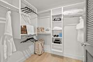 a walk in closet with white cabinets and shelves and a wicker basket