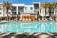 Pet-Friendly Apartments in Sacramento, CA - The Eisley - Swimming Pool with Lounge Tanning Chairs, Blue Umbrellas, Palms Trees, and Sundeck
