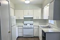 A white kitchen with a stove, sink, and cabinets.