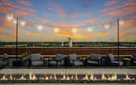 A fire pit sits in front of a row of chairs on a patio.