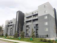A large grey apartment building with balconies and trees in front.