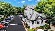 A white house with a grey roof is surrounded by a parking lot.