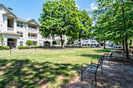 A park with a bench and trees in front of apartment buildings.