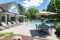 A pool area with a table and chairs and a house in the background.