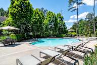 A pool surrounded by trees and lounge chairs.