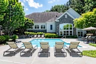 A pool surrounded by chairs and a house in the background.