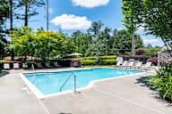 A swimming pool surrounded by trees and lawn chairs.