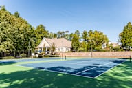 A tennis court surrounded by trees and a building in the background.
