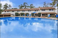 Large swimming pool in front of a building with a blue sky and trees in the background.