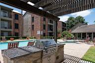 A grill is on a stone slab next to a pool.