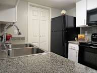 A kitchen with a black refrigerator and a granite countertop.