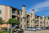 A row of apartment buildings with cars parked in front.