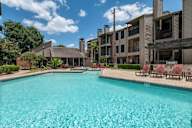 A large swimming pool in front of a building with a blue sky and clouds in the background.
