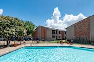 A swimming pool in front of a brick building with a fence and trees around it.