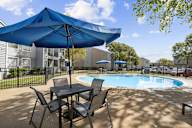 A blue umbrella is over a table and chairs by a pool.