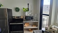 A kitchen with a refrigerator, oven, microwave, and a small shelf with utensils.