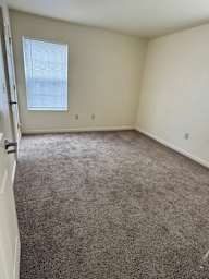 A room with a carpeted floor and a window with blinds.