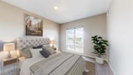 A bedroom with a large bed, a painting on the wall, and a potted plant.