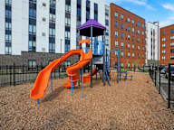 A playground with a purple and orange slide in front of apartment buildings.
