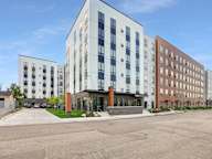 A modern multi-story building with a parking lot in front.