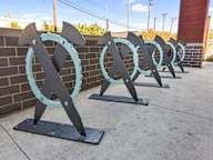 A series of black and turquoise horseshoe-shaped sculptures are displayed on a sidewalk.