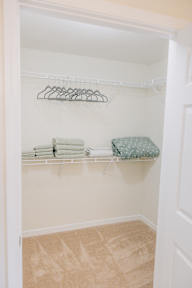 a walk in closet with white shelves and a green pillow