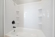 A white bathroom with a tub and shelves.