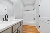 A white bathroom with a sink, mirror, and bathtub.