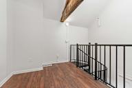 A room with a wooden beam on the ceiling and a black railing on the stairs.