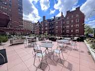 A patio with tables and chairs is surrounded by brick buildings.