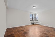A room with a brown floor and a window with blinds.
