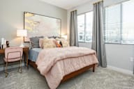A bedroom with a bed, desk, chair, and a large painting on the wall.