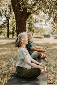 a man and a woman sitting on a yoga mat in a park