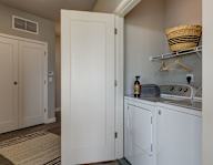 A white door is open to a small kitchen with a dishwasher and a basket on the shelf.