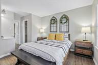 A bedroom with a bed, nightstands, and two windows with stained glass.
