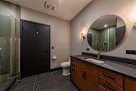 A bathroom with a black door, a white toilet, and a round mirror.