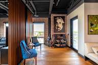 A room with a blue chair and a painting of a man's face on the wall.