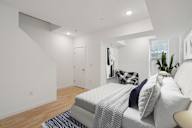 Compact bedroom with a comfortable bed with navy and white bedding, plush pillows, a white fluffy rug, and a plant by the window, creating a serene and inviting atmosphere.