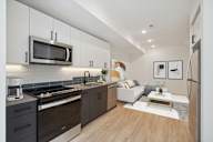 Chic open-concept living room with dark wood kitchen cabinets, stainless steel appliances, and a cozy lounge area with a light sofa, white marble coffee table, and stylish wall art.