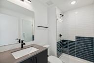 Sleek bathroom design featuring a vanity with a large mirror, white and navy blue tiles, and a shower-tub combo accented with modern fixtures.