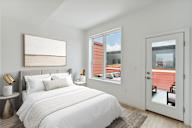 Compact bedroom with a comfortable bed with navy and white bedding, plush pillows, a white fluffy rug, and a plant by the window, creating a serene and inviting atmosphere.