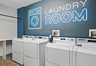 A row of washing machines in front of a wall with a neon sign that says Laundry Room.