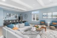 A modern living room with a grey sofa, a coffee table, and a kitchen area in the background.