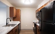 A kitchen with a black refrigerator and wooden cabinets at Hudson Heights Apartments, Mechanicville, NY