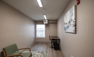 A room with a green chair, a desk, and a painting on the wall at Hudson Heights Apartments, Mechanicville, NY